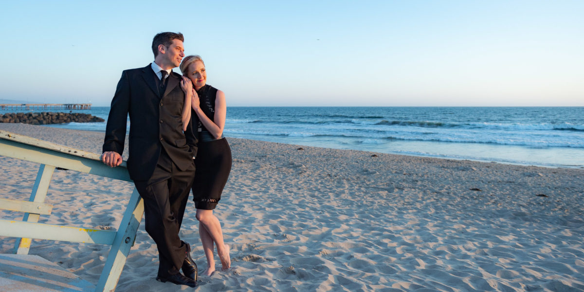 engagement photo of man and woman in formal attire on the beach.