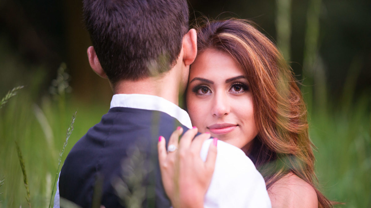 Engagement photo of man and woman in embrace. Woman looking over man's shoulder.