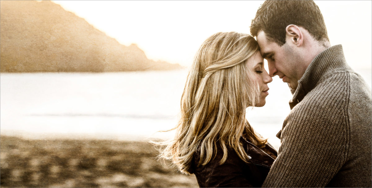 Engagement photo of young couple embracing at the beach.