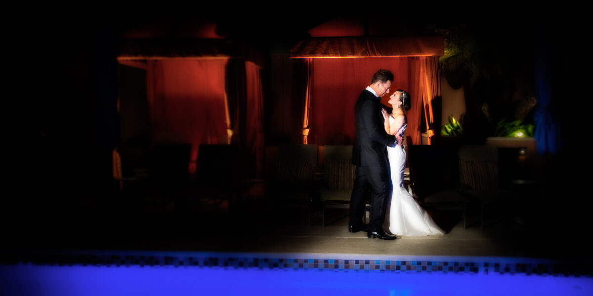 a bride and groom standing in front of a pool at night.
