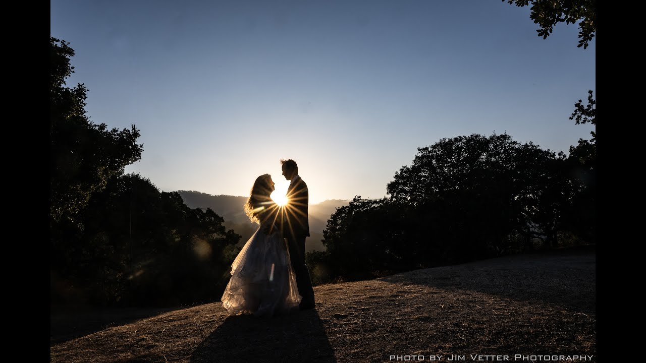 A bride and groom are silhouetted against the sun at sunset.