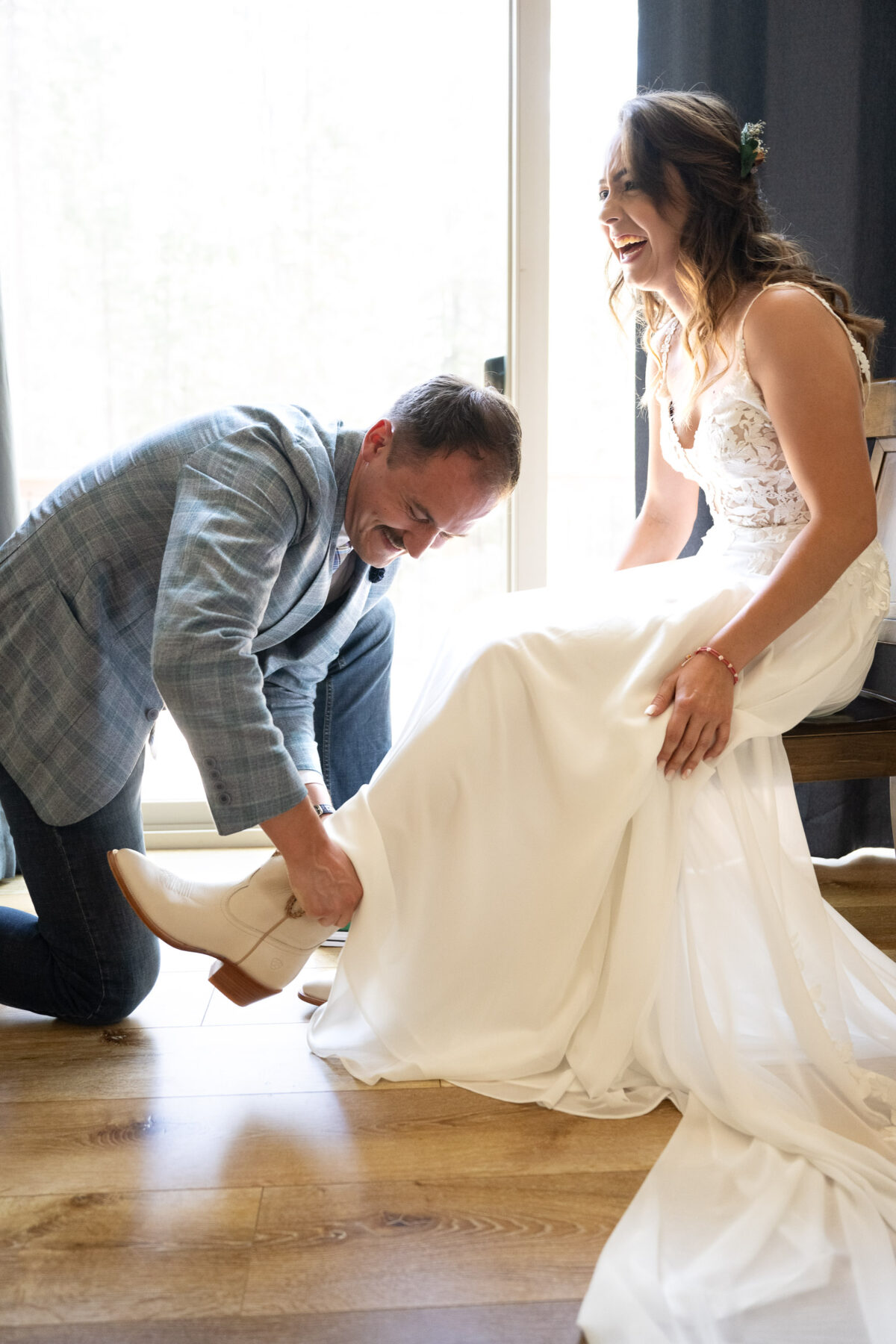 man putting wedding boots on bride laughter